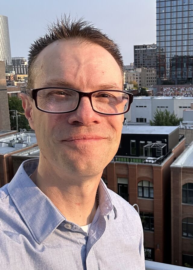Zach Ellerbrook on a rooftop, Chicago buildings behind him in late afternoon light.